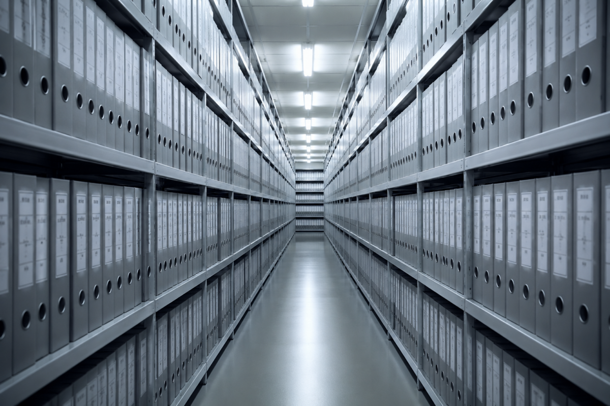 Des dossiers administratifs alignés de façon rigide sur des étagères métalliques d'archives.