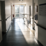 Perspective d'un couloir d'hôpital calme et dépouillé, baigné par la lumière du matin à travers une verrière.