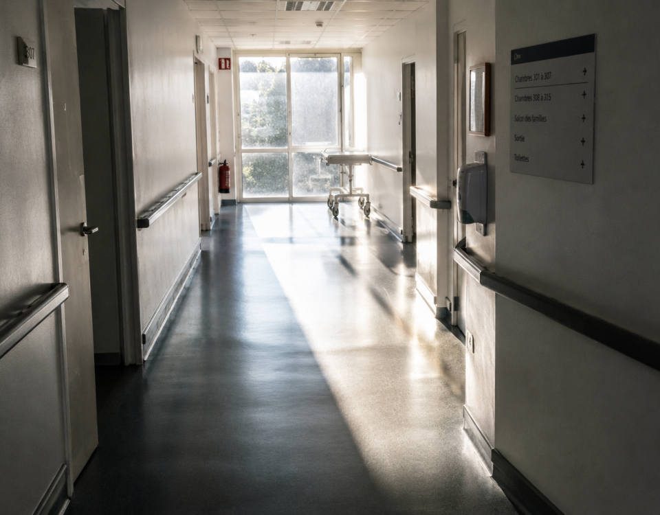 Perspective d'un couloir d'hôpital calme et dépouillé, baigné par la lumière du matin à travers une verrière.