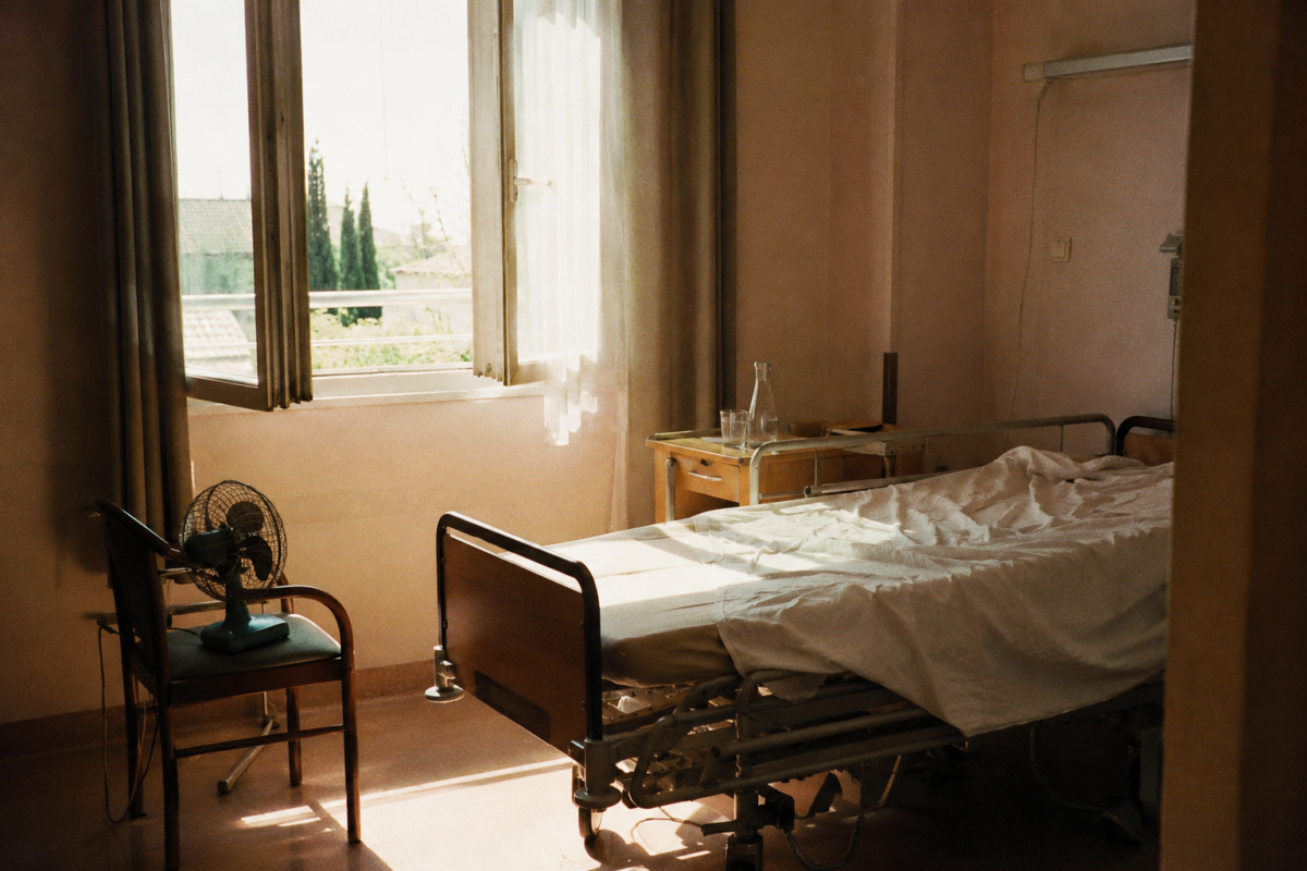 Chambre d’EHPAD vide en pleine canicule avec ventilateur, carafe d’eau et lit médicalisé.