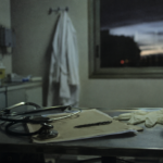 Table de soins avec stéthoscope, dossier médical et blouse suspendue dans une salle hospitalière.