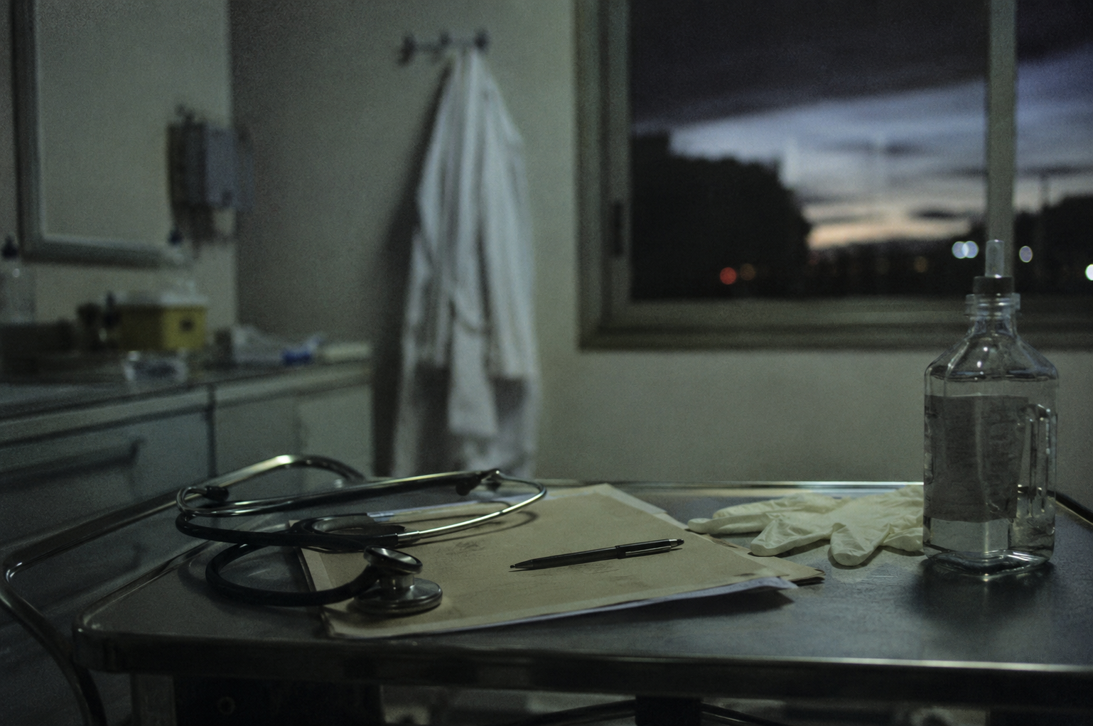 Table de soins avec stéthoscope, dossier médical et blouse suspendue dans une salle hospitalière.