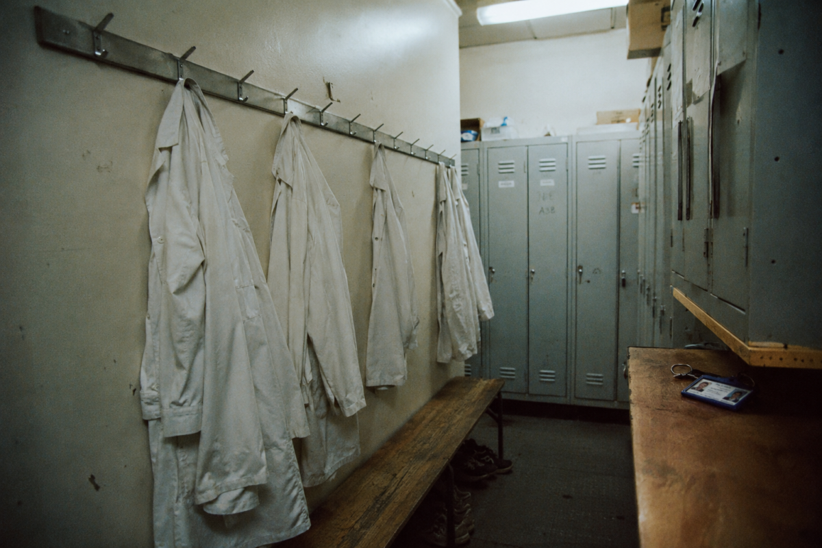 Vestiaire hospitalier avec blouses blanches suspendues et casiers gris en fin de service.