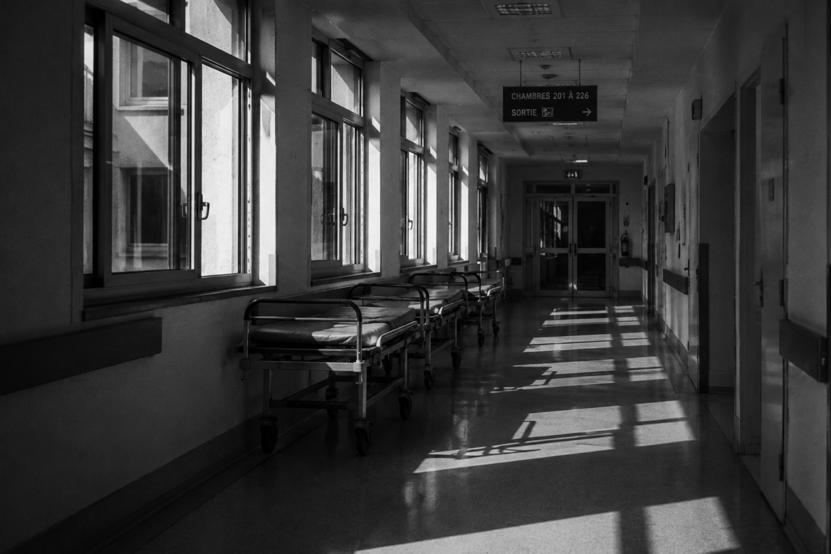 Un couloir d'hôpital vide et silencieux traversé par une lumière rasante.