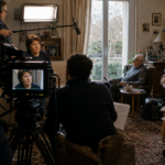 Une équipe de télévision filme une femme tandis que la photographie révèle une partie de la scène située hors du cadre de la caméra.