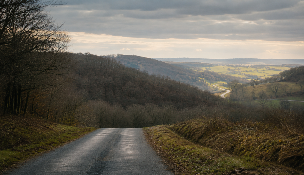 Une route disparaît derrière une colline avant de réapparaître plus loin dans une vallée éclairée.
