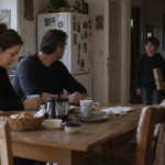 Un enfant entre dans une cuisine au moment où deux adultes interrompent leur conversation.