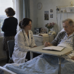 Un patient hospitalisé et perfusé tient un stylo au-dessus d’un agenda ouvert.