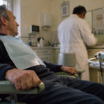 Un patient serre inconsciemment l’accoudoir d’un fauteuil tandis que son dentiste prépare le soin.