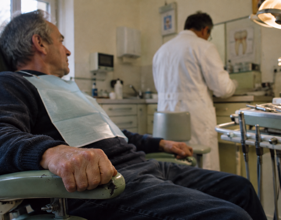 Un patient serre inconsciemment l’accoudoir d’un fauteuil tandis que son dentiste prépare le soin.