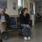Un homme malade attend une consultation aux côtés de sa fille, un carnet ouvert sur les genoux.