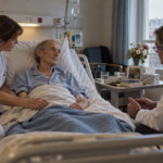 Un patient gravement malade et perfusé échange avec un médecin tandis qu’une infirmière prend soin de lui.